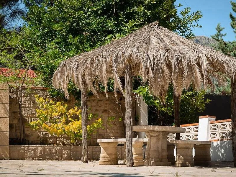 Palm-thatched shelter with stone benches and a table in the garden at La Vida Soñada